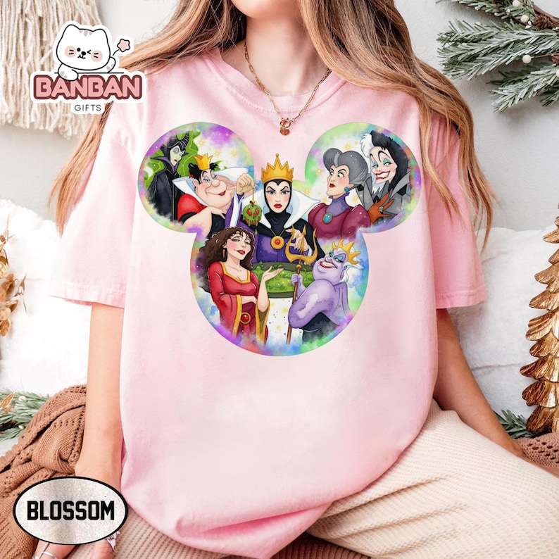 A person wearing a pink t-shirt with a colorful graphic of Disney villain characters from the Disney animated film series.