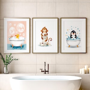 May include: Three framed wall art prints featuring watercolor illustrations: a yellow rubber duck in a white bathtub, a brown monkey holding toilet paper rolls, and a black and white penguin sitting in a white bathtub filled with blue water.