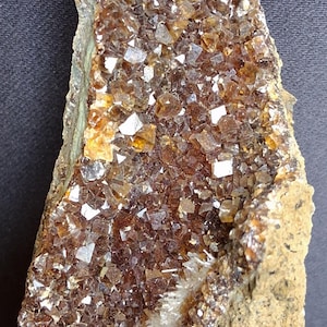 May include: A mineral specimen featuring a cluster of small, translucent, amber-brown crystals covering a textured, tan-colored rock matrix. A distinct, narrow band of fine, white, needle-like crystals runs vertically through the center of the formation.