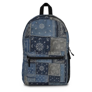May include: A backpack featuring a patchwork design of various blue and grey bandana patterns. The bag includes a black top handle, a front zippered pocket with a black zipper, and a black mesh side pocket. The overall aesthetic is a collage of prints.