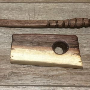 Puede incluir: Espátula y mantequera de madera tallada a mano. La espátula es larga y delgada con un mango tallado. La mantequera es rectangular con un agujero circular y un borde natural. Ambas son de madera marrón oscuro.