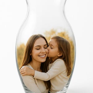 May include: A clear glass vase with a photograph inside. The photograph shows a woman smiling with her eyes closed, being kissed on the cheek by a young girl. Both are wearing light-colored sweaters.