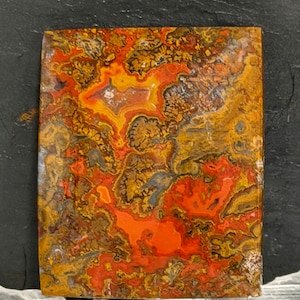 May include: A rectangular polished stone slab featuring a vibrant, intricate pattern of swirling colors including bright orange, deep red, golden yellow, and dark brown. The surface displays natural mineral inclusions and organic, vein-like textures.