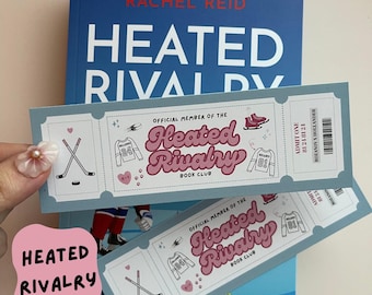 May include: A blue book titled "Heated Rivalry" with a matching bookmark. The bookmark is designed like a ticket, featuring hockey-themed illustrations and the text "Heated Rivalry Book Club."
