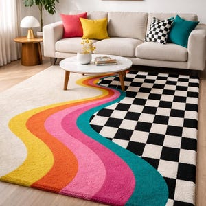 Modern hand-tufted wool area rug featuring bold retro-inspired flowing wave stripes in mustard yellow, burnt orange, blush pink, magenta, and teal that transition into a striking black and ivory checkerboard pattern. Displayed beneath a neutral sofa in a bright contemporary living room, this artistic statement rug complements Mid-Century Modern, Bauhaus, eclectic, and dopamine decor interiors.