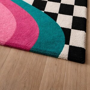 Premium wool hand-tufted rug designed with bold retro rainbow waves in golden yellow, orange, blush pink, magenta, and teal alongside a high-contrast black and white checkerboard pattern. This unique statement rug combines modern geometric design with soft handcrafted texture, making it ideal for contemporary living rooms, bedrooms, studios, and stylish apartment interiors.