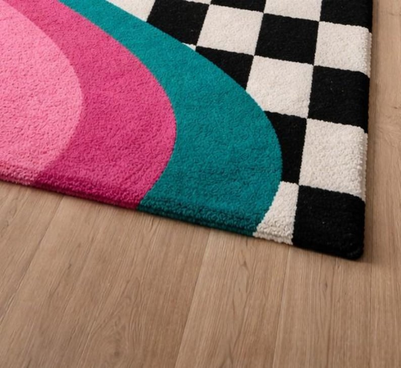 Premium wool hand-tufted rug designed with bold retro rainbow waves in golden yellow, orange, blush pink, magenta, and teal alongside a high-contrast black and white checkerboard pattern. This unique statement rug combines modern geometric design with soft handcrafted texture, making it ideal for contemporary living rooms, bedrooms, studios, and stylish apartment interiors.