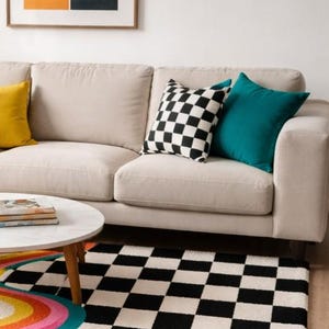 Handmade wool area rug showcasing an eye-catching retro wave design with flowing mustard, orange, pink, magenta, and teal curves merging into a bold black and white checkerboard pattern. The plush hand-tufted construction creates a soft, luxurious feel underfoot while enhancing modern, maximalist, Bauhaus, eclectic, and artistic interior spaces with vibrant visual appeal.