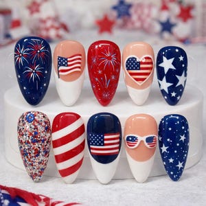 May include: A set of ten artificial nails with patriotic designs. The nails feature various designs, including fireworks, the American flag, stars, and stripes, in red, white, and blue colors. The nails are oval-shaped and have a glossy finish.