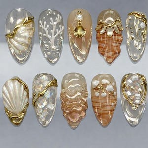 May include: A collection of ten acrylic nail designs featuring various ocean-themed embellishments. Each nail showcases a unique design, including gold accents, seashells, coral, and pearl details, all set against a clear or translucent base.