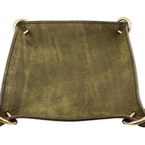 Könnte beinhalten: Olivgrünes Leder-Tablett mit goldfarbenen Metallringgriffen. Das Tablett hat eine Used-Optik und ist mit dunklem Faden genäht. Die Ecken sind mit kleinen Metallnieten verstärkt.