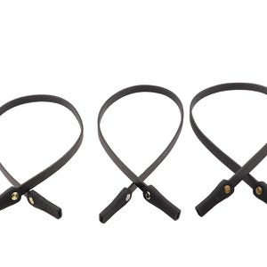Puede incluir: Tres correas de gafas de cuero negro con remaches dorados. Cada correa est&aacute; en bucle y tiene un peque&ntilde;o extremo rectangular. Las correas se muestran sobre un fondo blanco.