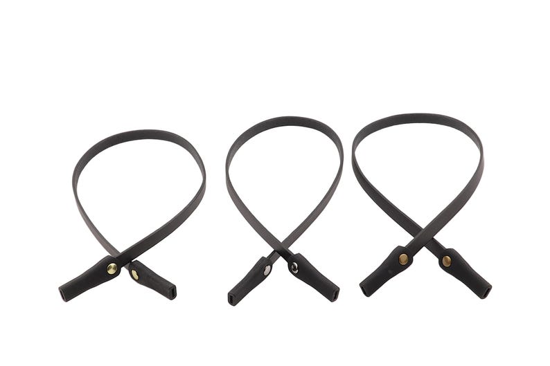 Puede incluir: Tres correas de gafas de cuero negro con remaches dorados. Cada correa est&aacute; en bucle y tiene un peque&ntilde;o extremo rectangular. Las correas se muestran sobre un fondo blanco.