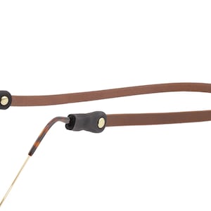 Puede incluir: Una correa de gafas de cuero marr&oacute;n con extremos de goma negra y remaches dorados. La correa est&aacute; dise&ntilde;ada para sujetar las gafas y evitar que se caigan. Las gafas tienen un patr&oacute;n de carey.