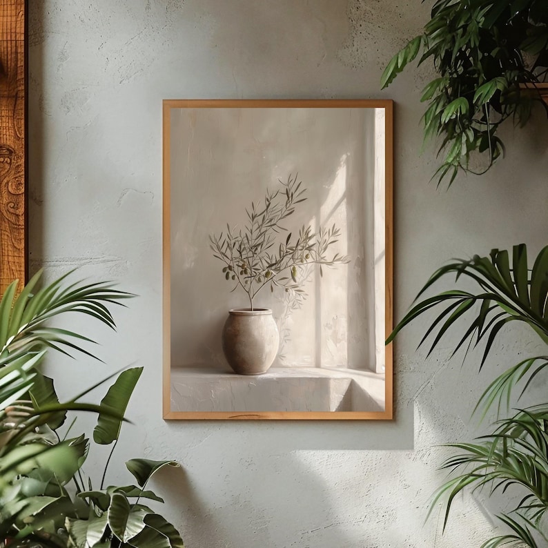 Op de afbeelding: Een ingelijste print met een olijftak in een beige keramische vaas. Het kunstwerk staat tegen een neutrale achtergrond met zachte verlichting, wat een serene en minimalistische esthetiek cre&euml;ert. De lijst is lichtbruin.