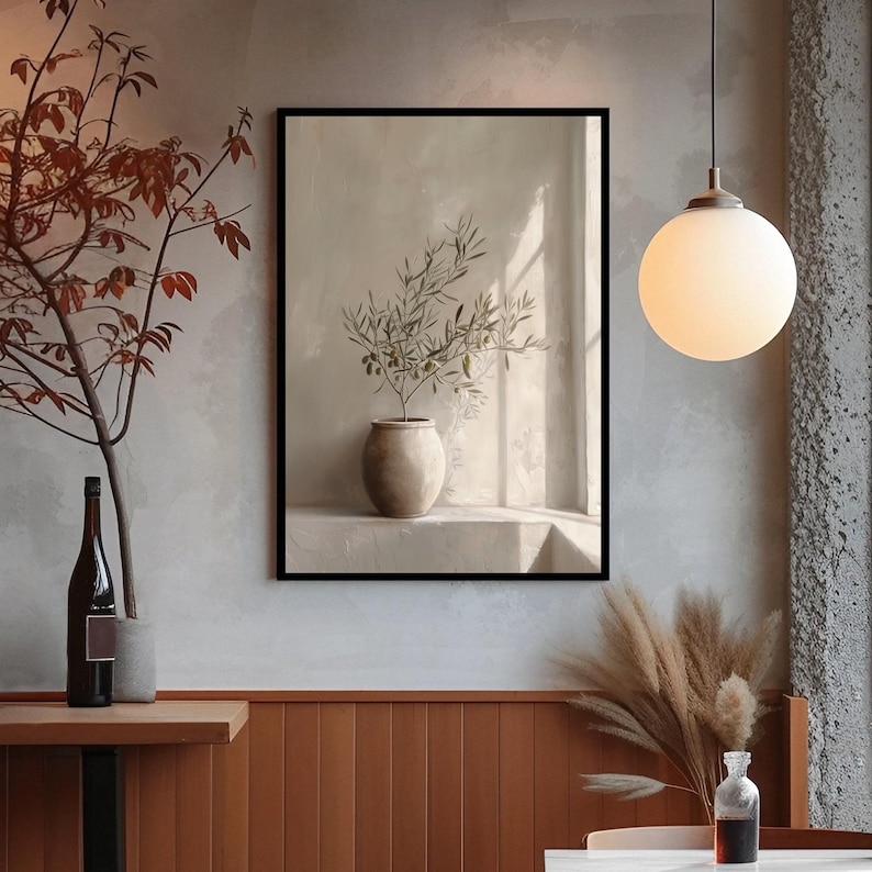 Op de afbeelding: Een ingelijste kunstdruk met een stilleven van een vaas met olijftakken. Het kunstwerk is in een neutraal kleurenpalet, met een beige vaas en een lichte achtergrond. De print wordt getoond in een kamer met een warme sfeer.