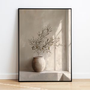 Op de afbeelding: Een ingelijste print met een olijftak in een beige keramische pot. Het kunstwerk heeft een neutraal kleurenpalet met zachte schaduwen en een minimalistische esthetiek. De olijftak heeft groene olijven en bladeren.