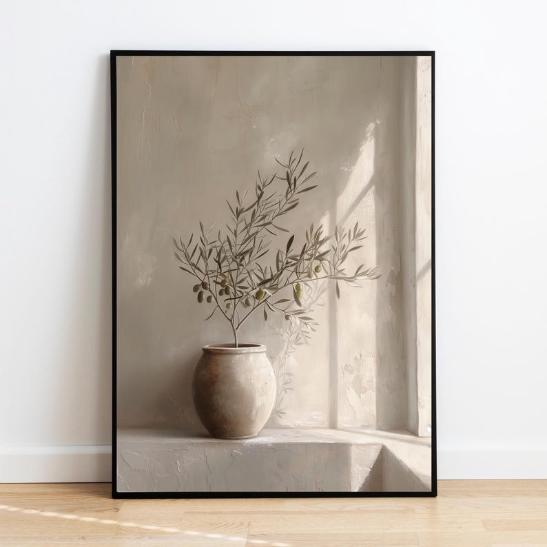 Op de afbeelding: Een ingelijste print met een olijftak in een beige keramische pot. Het kunstwerk heeft een neutraal kleurenpalet met zachte schaduwen en een minimalistische esthetiek. De olijftak heeft groene olijven en bladeren.