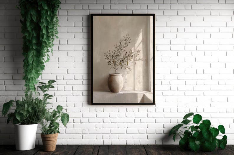 Op de afbeelding: Een ingelijste kunstdruk met olijftakken in een beige vaas. Het kunstwerk staat tegen een neutrale achtergrond met zachte verlichting. De print wordt weergegeven op een witte bakstenen muur, met planten in potten op de voorgrond.