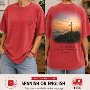 Puede incluir: Una camiseta roja de manga corta con una pequeña cruz negra y el texto Con Dios nada me faltará en el frente. La parte posterior muestra un paisaje montañoso con una cruz al atardecer y el texto Todo lo puedo en Cristo que me fortalece.