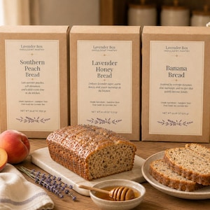 May include: Three rectangular cardboard boxes labeled Lavender Box Indulgent Pantry containing Southern Peach Bread, Lavender Honey Bread, and Banana Bread, each weighing 20.18 oz. A loaf of bread, sliced bread, a peach, and honey are displayed.