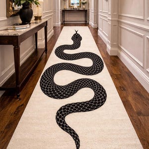 Puede incluir: Una alfombra de pasillo color crema con un gran diseño de serpiente negra. La serpiente está representada con un patrón de escamas detallado. La alfombra está colocada en un pasillo con suelo de madera oscura y paredes blancas.