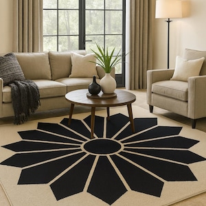 May include: A living room scene featuring a beige sofa, armchair, and a round wooden coffee table. A large area rug with a black floral design dominates the floor. A floor lamp and window with curtains complete the room.