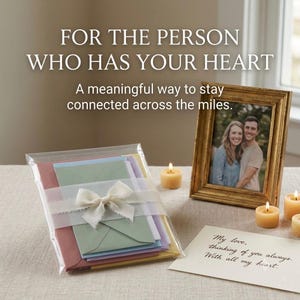 May include: A stack of colourful envelopes in a clear plastic sleeve tied with a white ribbon, a gold picture frame containing a photograph of a couple, three small round candles, and a handwritten note that reads My love, thinking of you always.
