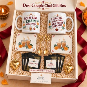 May include: A Desi Couple Chai Gift Box containing two white ceramic mugs with printed text and floral motifs, two square coasters, two gold-toned leaf-shaped spoons, two heart-shaped tea infusers, and eight tea sachets labeled Masala Chai and Rose Black Tea.