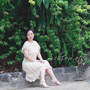 May include: A woman in a cream-coloured, crocheted dress with short sleeves and a knee-length hem. She is sitting on a stone ledge in front of lush green foliage. The image includes the text "chieu.etsy.com".
