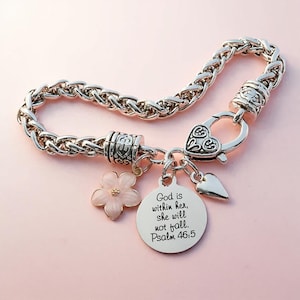 May include: Silver-toned bracelet with a woven chain design. The bracelet features a heart-shaped clasp and charms, including a pink flower, a small heart, and a round pendant with the text "God is within her, she will not fall. Psalm 46:5."
