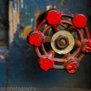 May include: A red metal valve with six spokes and a round center. The valve is rusty and has a worn, faded red paint finish.