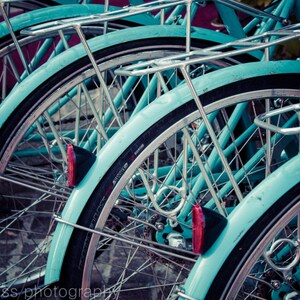 Puede incluir: Primer plano de tres bicicletas de color azul turquesa con manillares plateados y detalles cromados. Las bicicletas están apiladas una encima de la otra, con la rueda delantera de la bicicleta superior visible.