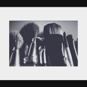 May include: A grayscale photograph of several makeup brushes, with varying sizes and shapes. The bristles are visible, and the handles are partially obscured. The image is framed with a white border and a black background. The text "jessica weiss photography" is visible.