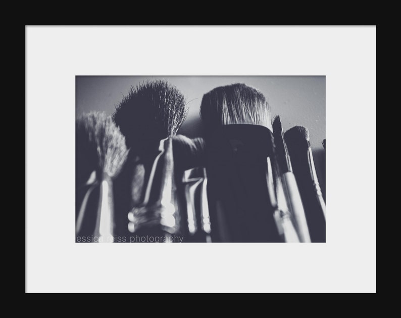 May include: A grayscale photograph of several makeup brushes, with varying sizes and shapes. The bristles are visible, and the handles are partially obscured. The image is framed with a white border and a black background. The text "jessica weiss photography" is visible.