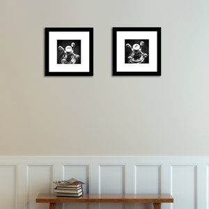 May include: Two black and white framed photographs of a vintage faucet handle with the word "COLD" on the knob. The photos are hanging on a white wall above a wooden bench.