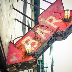 May include: A red and white sign with the word "BAR" painted on it. The sign is attached to a building and has two light fixtures on it.