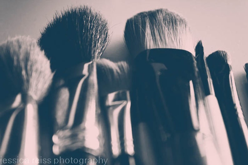 May include: Close-up of several makeup brushes with black handles and soft bristles. The image has a sepia tone, with the brushes arranged closely together. The text "jessica reiss photography" is visible at the bottom.