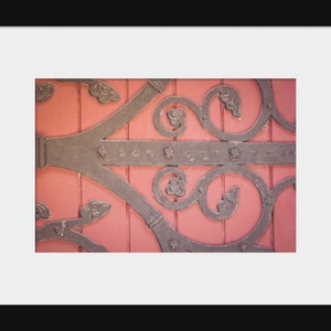 May include: Close-up of a decorative metal door hinge with intricate scrollwork, set against a vibrant pink wooden door.
