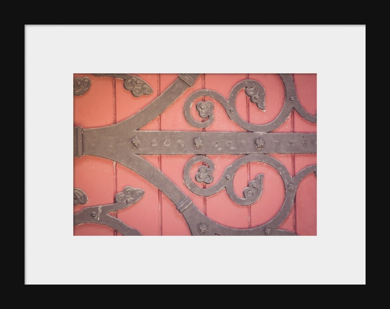 May include: Close-up of a decorative metal door hinge with intricate scrollwork, set against a vibrant pink wooden door.