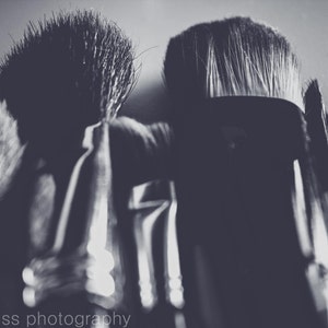 May include: A grayscale image of several makeup brushes. The brushes vary in size and shape, with soft bristles and dark handles. The image is well-lit, highlighting the textures and forms of the brushes, suitable for applying cosmetics.