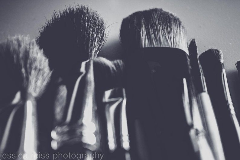 May include: A grayscale image of several makeup brushes. The brushes vary in size and shape, with soft bristles and dark handles. The image is well-lit, highlighting the textures and forms of the brushes, suitable for applying cosmetics.