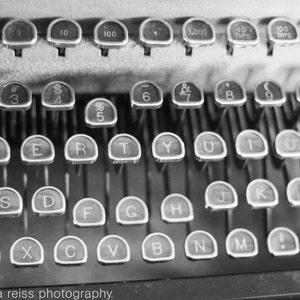 May include: Black and white image of a vintage typewriter with keys labelled with letters, numbers, and symbols. The keys are arranged in a standard QWERTY layout.