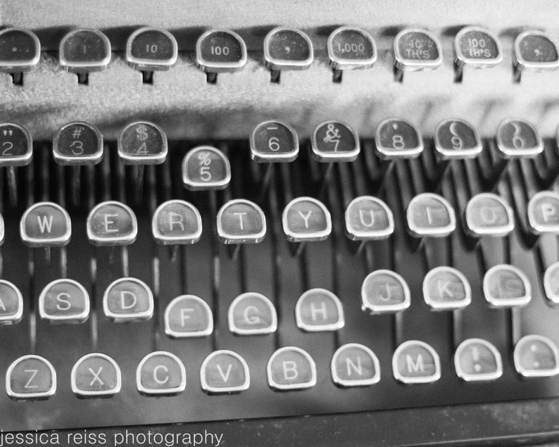 May include: Black and white image of a vintage typewriter with keys labelled with letters, numbers, and symbols. The keys are arranged in a standard QWERTY layout.