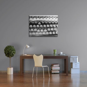 May include: A black and white photograph of a vintage typewriter keyboard. The keys are worn and have a faded look. The image is displayed on a wall above a desk with a chair, a lamp, and a potted plant.