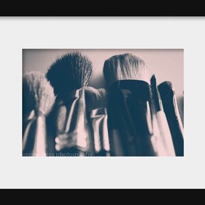 May include: Close-up of a collection of makeup brushes with dark handles and soft bristles. The brushes are arranged closely together, with the bristles facing upwards. The image has a soft, muted color palette, with a focus on texture and detail. The text "jessica weiss photography" is visible.