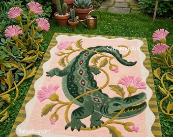 May include: A rectangular tufted rug featuring a central dark green crocodile illustration surrounded by pink flowers and winding stems on a light pink background, framed by a scalloped white border and a striped olive green and yellow edge.