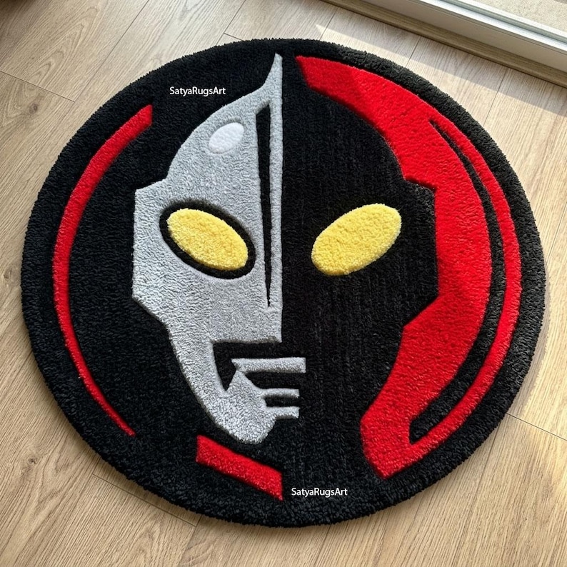 Pu&ograve; includere: Un tappeto rotondo con un design di personaggio stilizzato in nero, argento, rosso e giallo. Il design &egrave; simmetrico, con un volto argentato a sinistra e un volto nero a destra, bordato di rosso. Il tappeto ha una consistenza morbida.