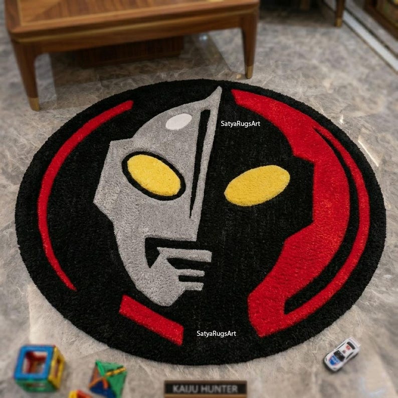 Pu&ograve; includere: Un tappeto rotondo nero con un design di personaggio stilizzato in grigio, giallo e rosso. Il design include il testo "SatyaRugsArt" e "KAUU HUNTER". Il tappeto &egrave; posto su un pavimento effetto marmo.