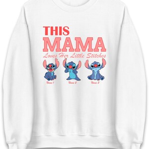 May include: White sweatshirt with the text "THIS MAMA" in red and pink lettering. Below the text are three blue cartoon characters with the text "Name 1", "Name 2", and "Name 3" below each character. The text "Loves Her Little Stitches" is below the word "MAMA".
